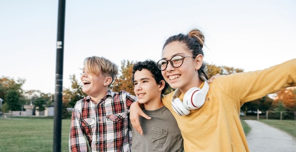 accounts-for-kids Three smiling kids standing together outdoors, with one wearing glasses and headphones, enjoying a sunny day at the park
